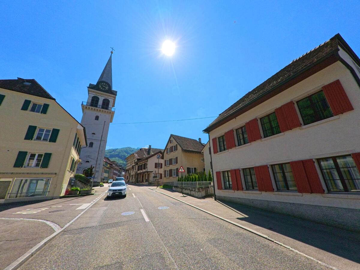  In Waldenburg (4437, Kanton Baselland) prägt der markante Kirchturm mit Uhr das Ortsbild entlang einer sanft ansteigenden Strasse mit traditionellen Wohnhäusern.