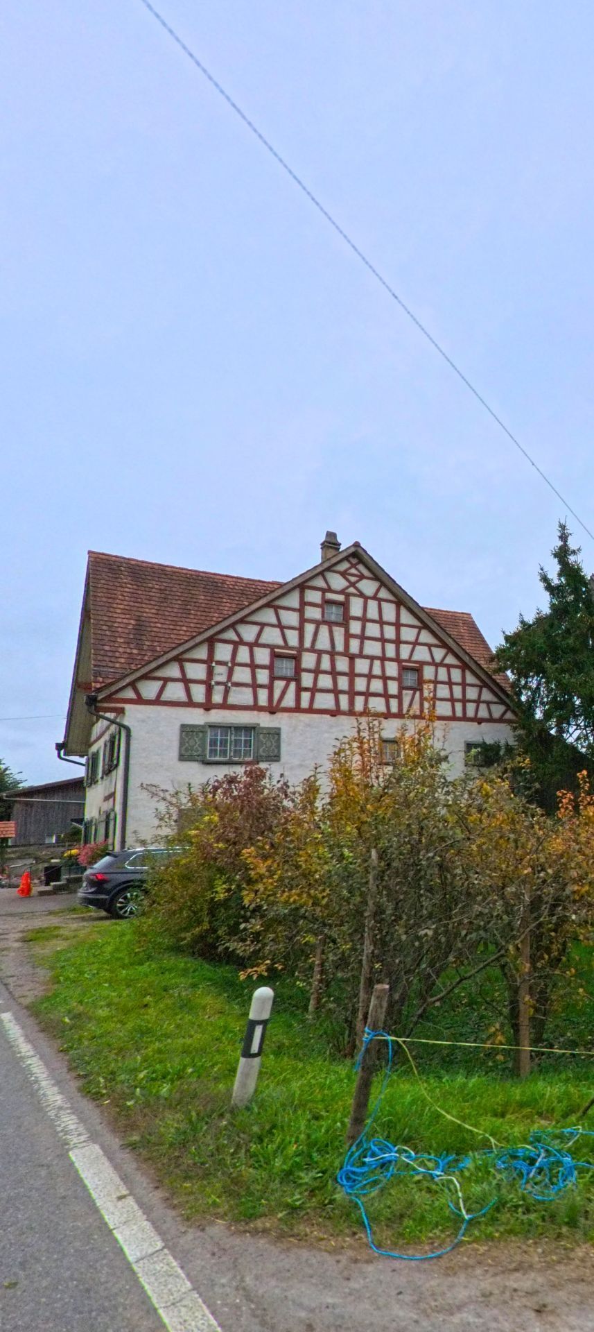 Am Strassenrand in Waldkirch (9205, Kanton St. Gallen) steht ein traditionelles Fachwerkhaus mit Ziegeldach, umgeben von Gruenflaeche und Hecken.