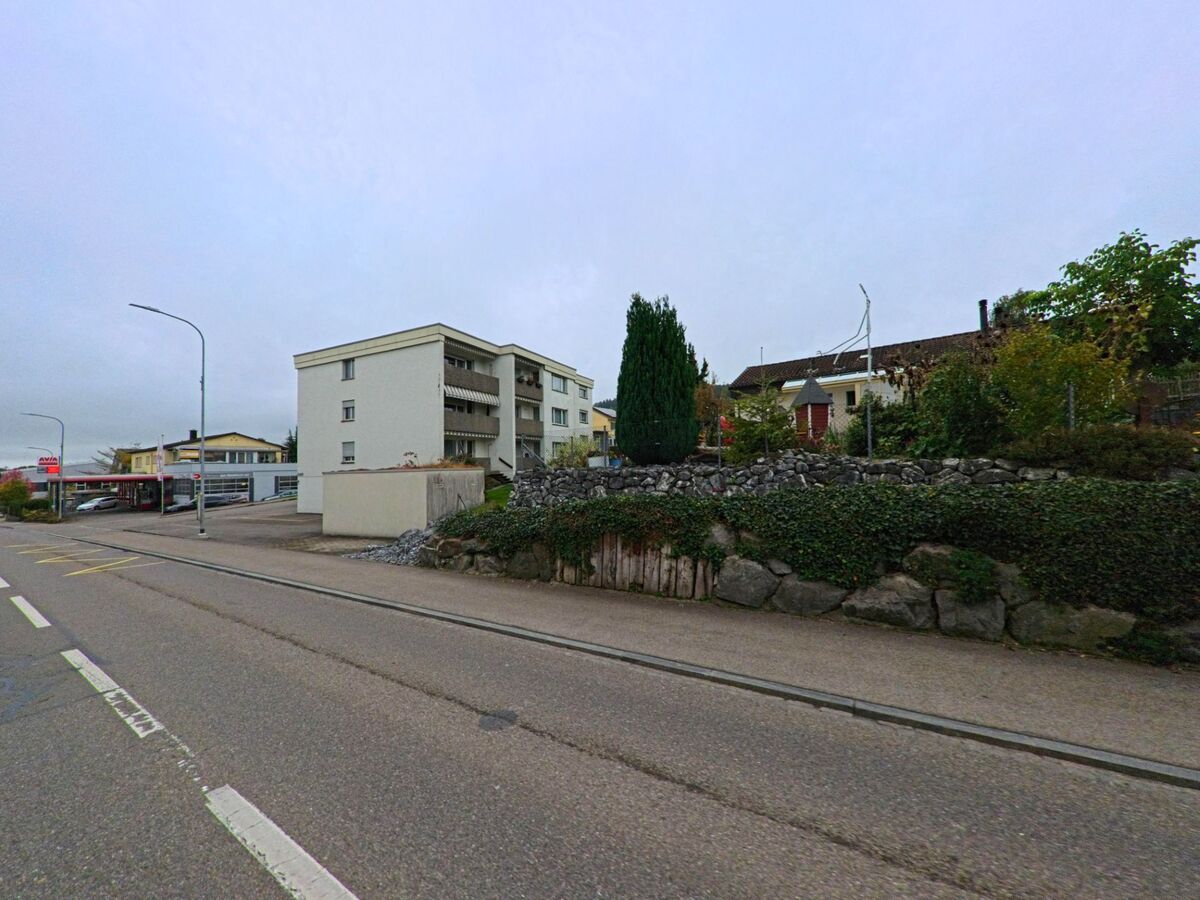 Nahe eines Mehrfamilienhauses in Waldkirch (9205, Kanton St. Gallen) verlaeuft eine Ortsstrasse mit Gehweg, Steinmauer und angrenzender Wohnbebauung.