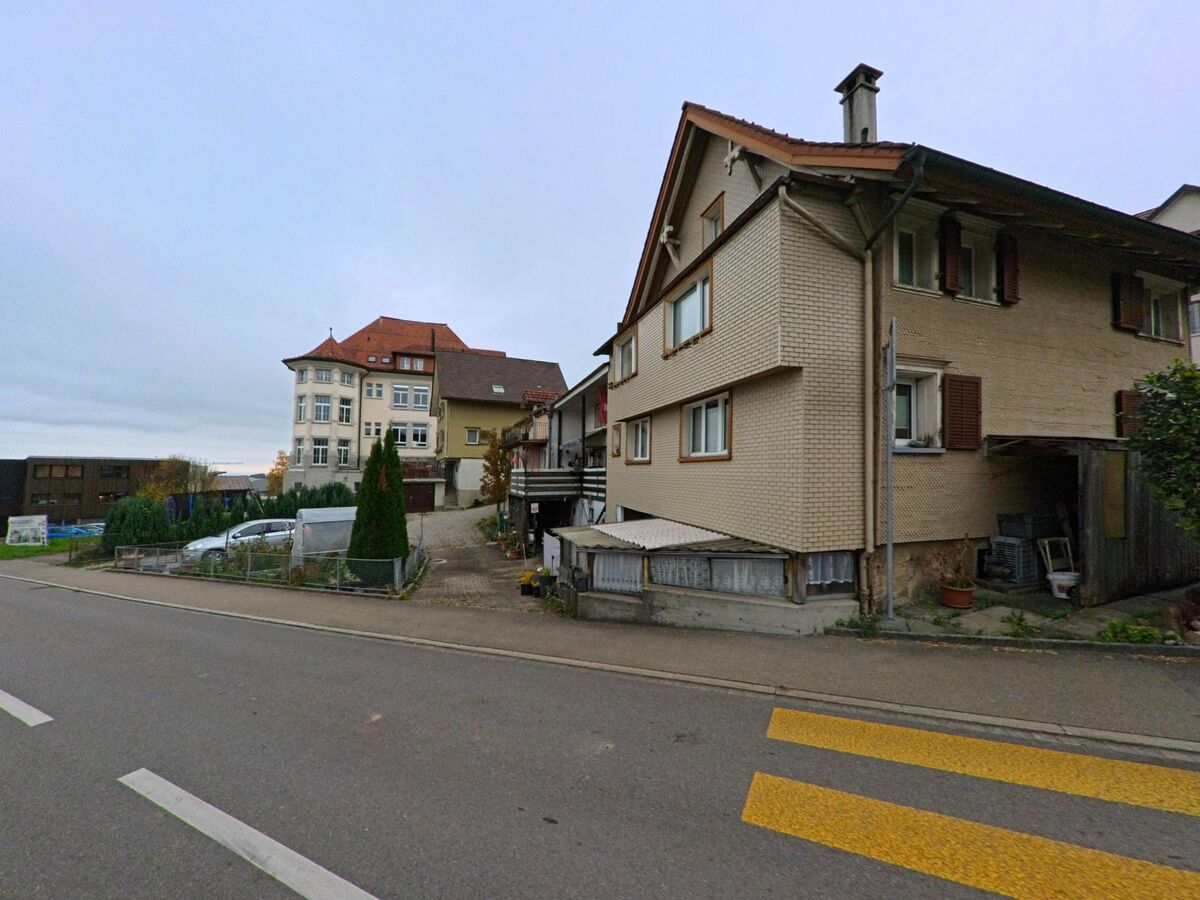 An einer Wohnstrasse in Waldkirch (9205, Kanton St. Gallen) stehen mehrgeschossige Wohnhaeuser entlang eines schmalen Gehwegs mit Blick auf weitere Gebaeude.