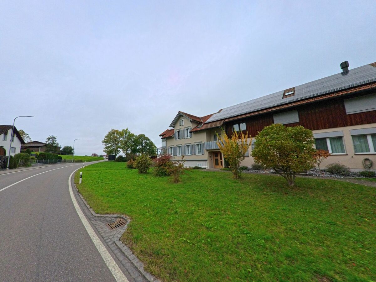 An einer leicht ansteigenden Strasse in Waldkirch (9205, Kanton St. Gallen) liegen Wohnhaeuser mit Vorgarten, Solaranlage und angrenzender Gruenflaeche.