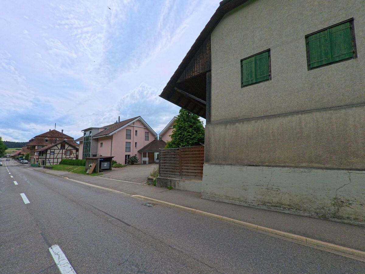 Entlang der Hauptstrasse in Walkringen (3512, Kanton Bern) stehen moderne Wohnhäuser neben traditionellen Fachwerkbauten und einer Bushaltestelle.