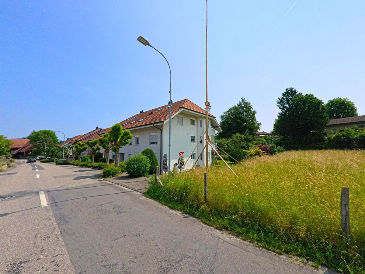 In Walliswil bei Wangen (3377, Kanton Bern) führt eine Straße entlang von modernen Häusern, mit einem grünen Wiesenbereich und einem Strommast im Vordergrund.