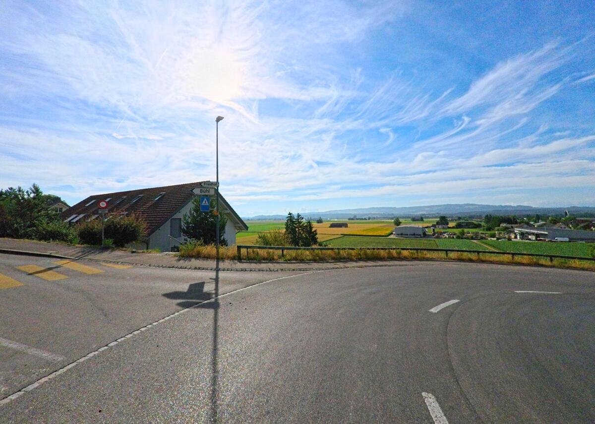 In Walperswil (3275, Kanton Bern) bietet eine Kurve auf erhöhter Strasse einen weiten Blick über Felder und das Mittelland bis zum Horizont.