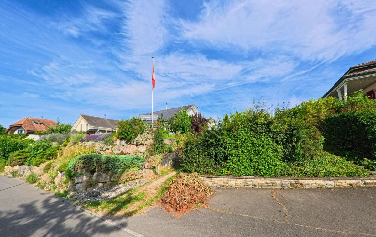 In Walperswil (3275, Kanton Bern) stehen Einfamilienhäuser auf einer kleinen Anhöhe mit gepflegtem Garten, Sträuchern und einer Schweizer Flagge im Vorgarten.