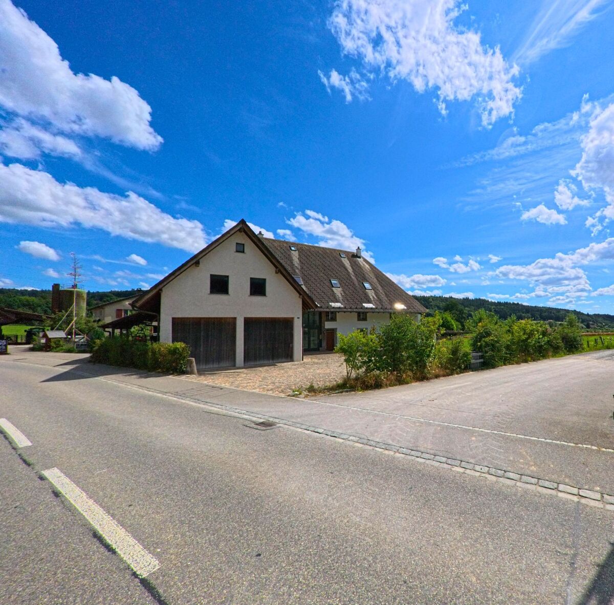 Ein modernes Wohnhaus mit grosszügiger Einfahrt und Garage steht am Strassenrand von Walterswil (5746, Kanton Solothurn) vor einer offenen Landschaft mit Wiesen und Wald.