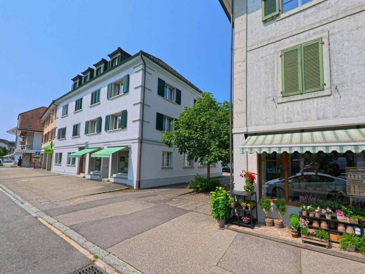 In der Ortsmitte von Wangen an der Aare (3380, Kanton Bern) reihen sich ein Blumenladen und eine Apotheke mit grünen Fensterläden an einer ruhigen Strasse.