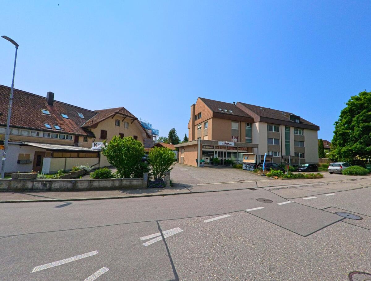 An einer Kreuzung in Wangen an der Aare (3380, Kanton Bern) befinden sich ein Wohn- und Geschäftshaus mit Coiffeursalon sowie ältere Nachbargebäude.