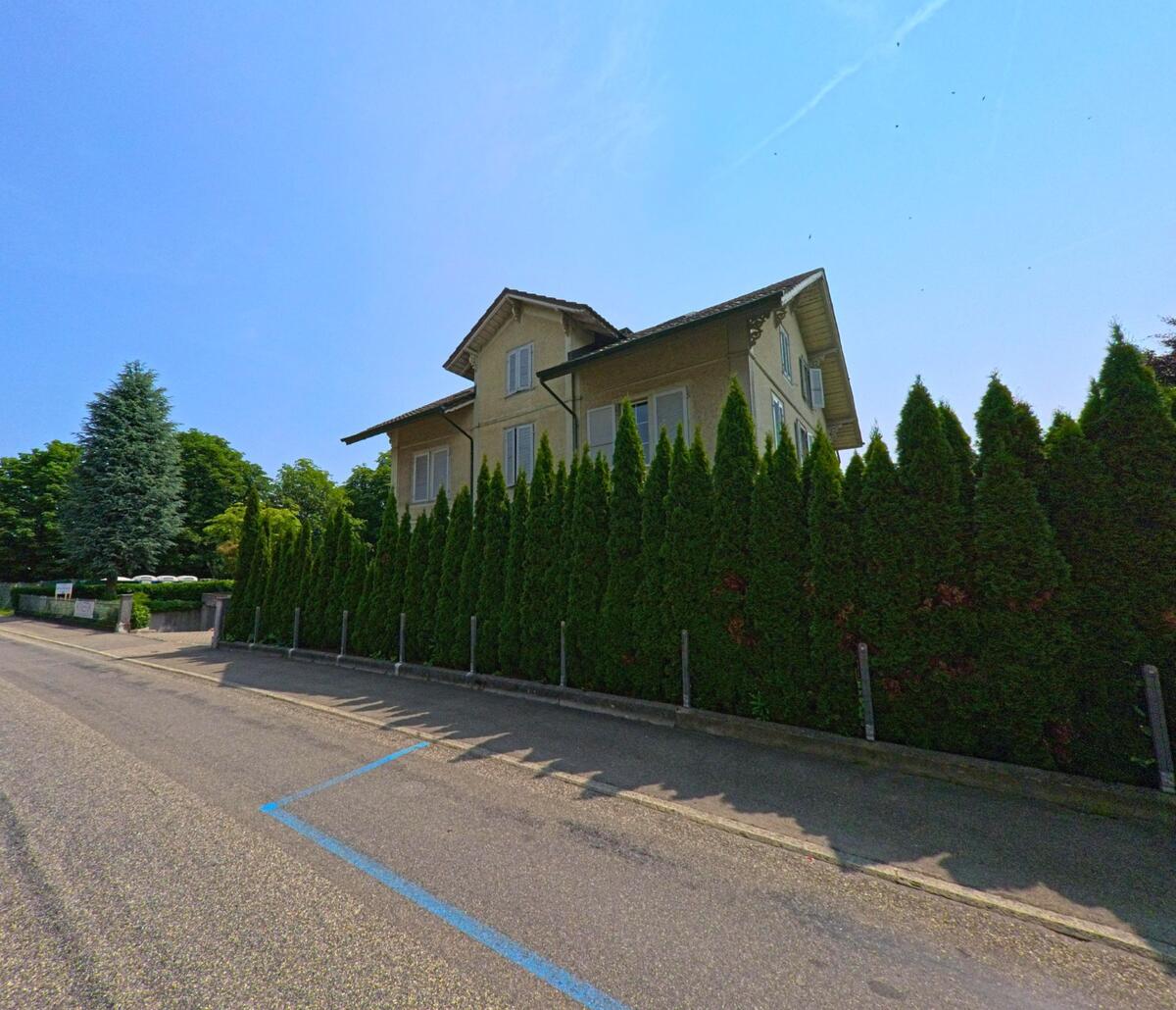 In Wangen an der Aare (3380, Kanton Bern) steht ein Wohnhaus mit hellen Fensterläden hinter einer dichten Reihe hoher Lebensbäume an einer Nebenstrasse.