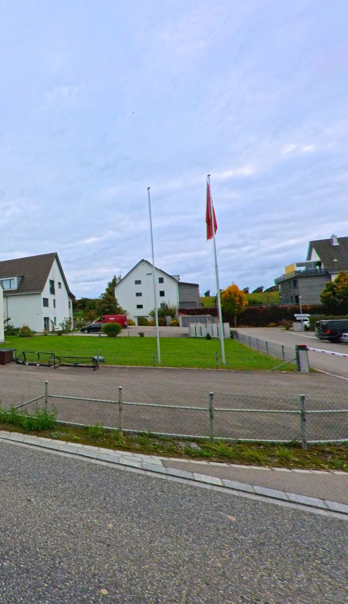 Auf einer gepflegten Gruenflaeche mit Fahnenmasten liegen Wohngebaeude und Zufahrten in Warth-Weiningen (8532, Kanton Thurgau) bei ruhiger Alltagsstimmung.