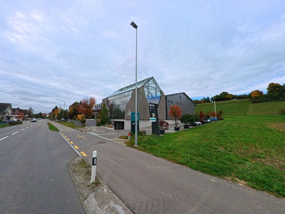 Ein modernes Gebaeude mit Glasfassade liegt an einer Hauptstrasse neben einer Gruenflaeche in Warth-Weiningen (8532, Kanton Thurgau) bei ruhiger Verkehrslage.