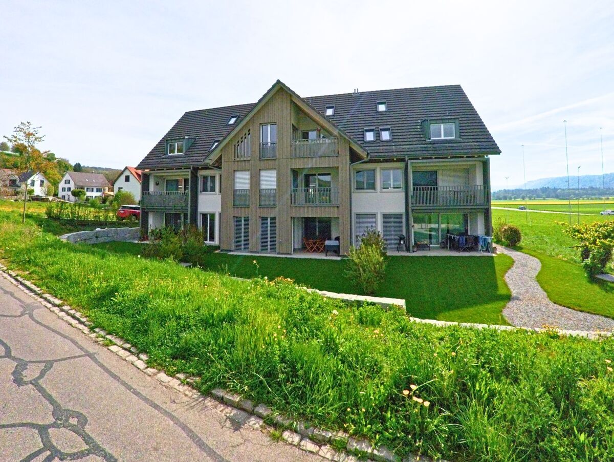 Am südlichen Rand von Wasterkingen (PLZ 8195, Kanton Zürich) liegt ein modernes Mehrfamilienhaus mit Blick auf offene Felder und eine ruhige Seitenstrasse.