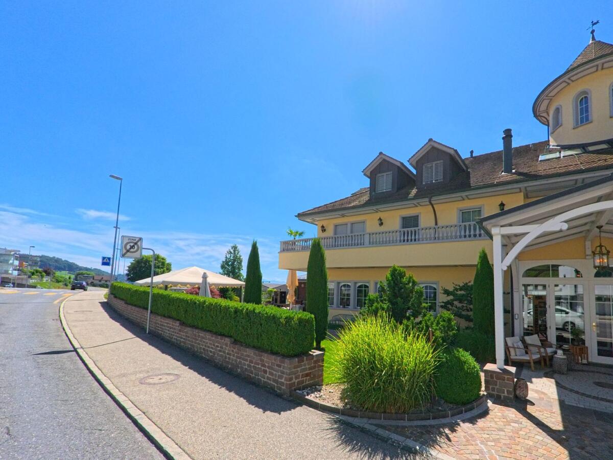 In Wauwil (PLZ 6242, Kanton Luzern) befindet sich ein eindrucksvolles Gebaeude mit Rundturm und ueberdachtem Eingang, umgeben von Zierstraeuchern und Kopfsteinpflaster.