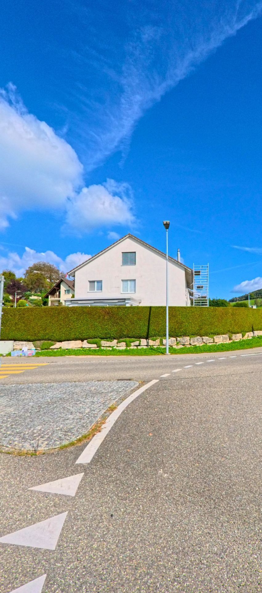 Ein Einfamilienhaus in Wegenstetten (4317, Kanton Aargau) steht auf einer Anhöhe hinter einer geschnittenen Hecke an einer leicht einbiegenden Strasse.