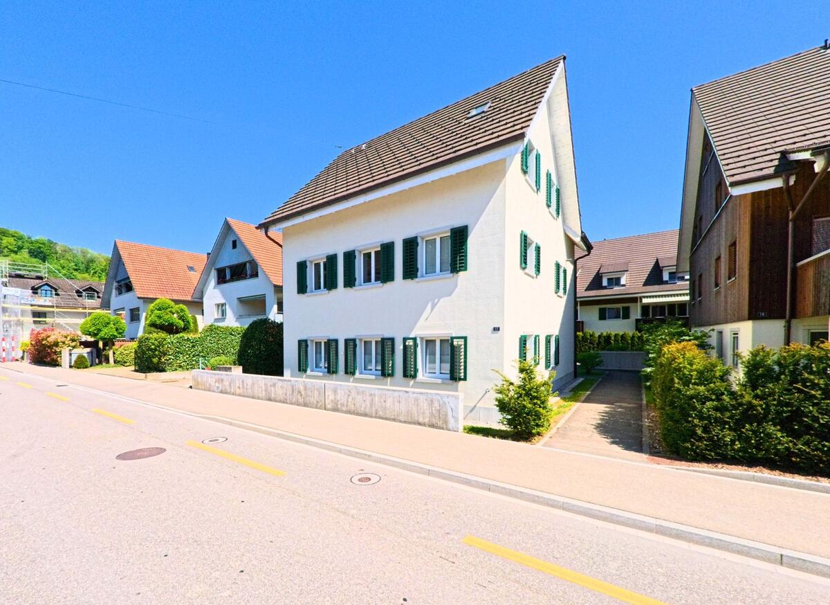In einer Wohnstrasse von Weiningen (8104, Kanton Zürich) reihen sich gepflegte Einfamilienhäuser mit Vorgärten und Fensterläden aneinander.