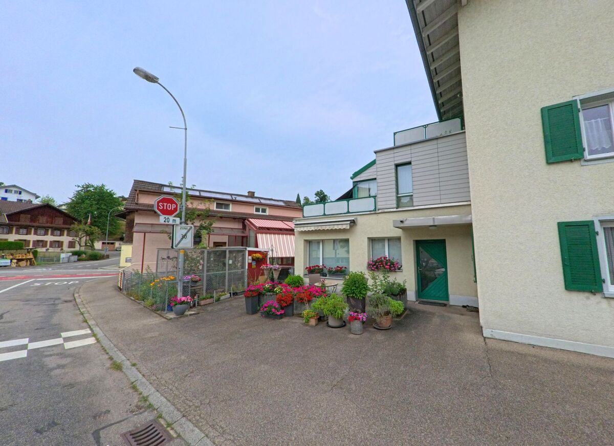  In Werthenstein (6106, Kanton Luzern) befindet sich vor einem Wohnhaus mit gruener Tuer und Fensterlaeden eine bunt bepflanzte Terrasse, nahe einer Nebenstrasse mit Stoppschild.