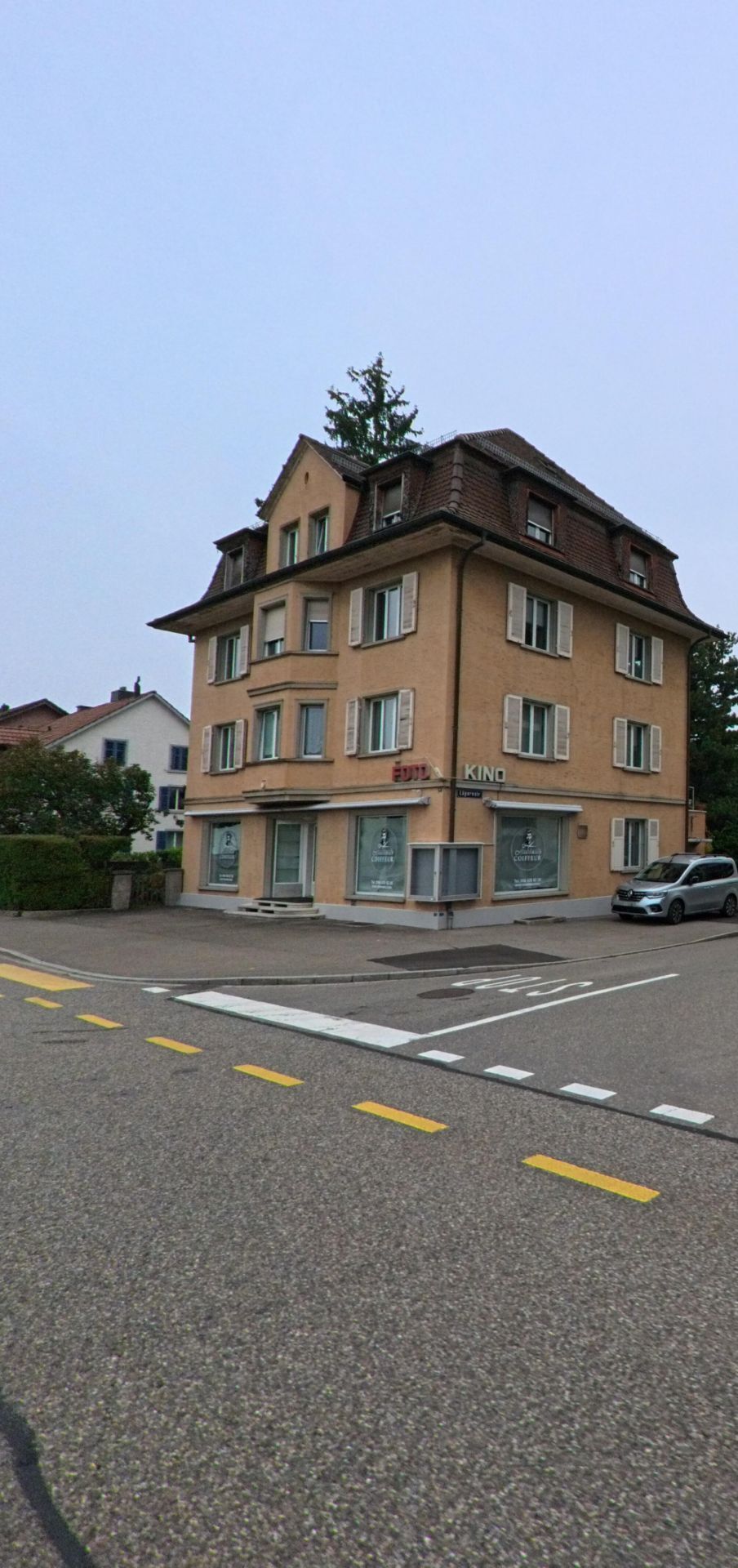Ein mehrgeschossiges Wohnhaus mit Ladenfronten an einer Kreuzung praegt in Wettingen (5430, Kanton Aargau) das ruhige Quartierbild.