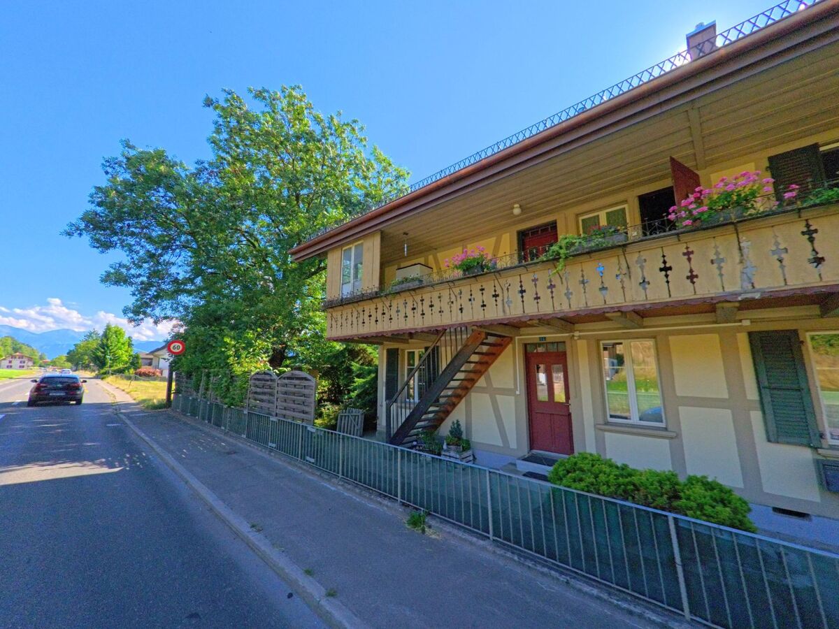 In Wichtrach (3114, Kanton Bern) steht ein traditionelles Wohnhaus mit verziertem Holzbalkon und bunten Blumenkästen direkt an einer verkehrsarmen Landstrasse.