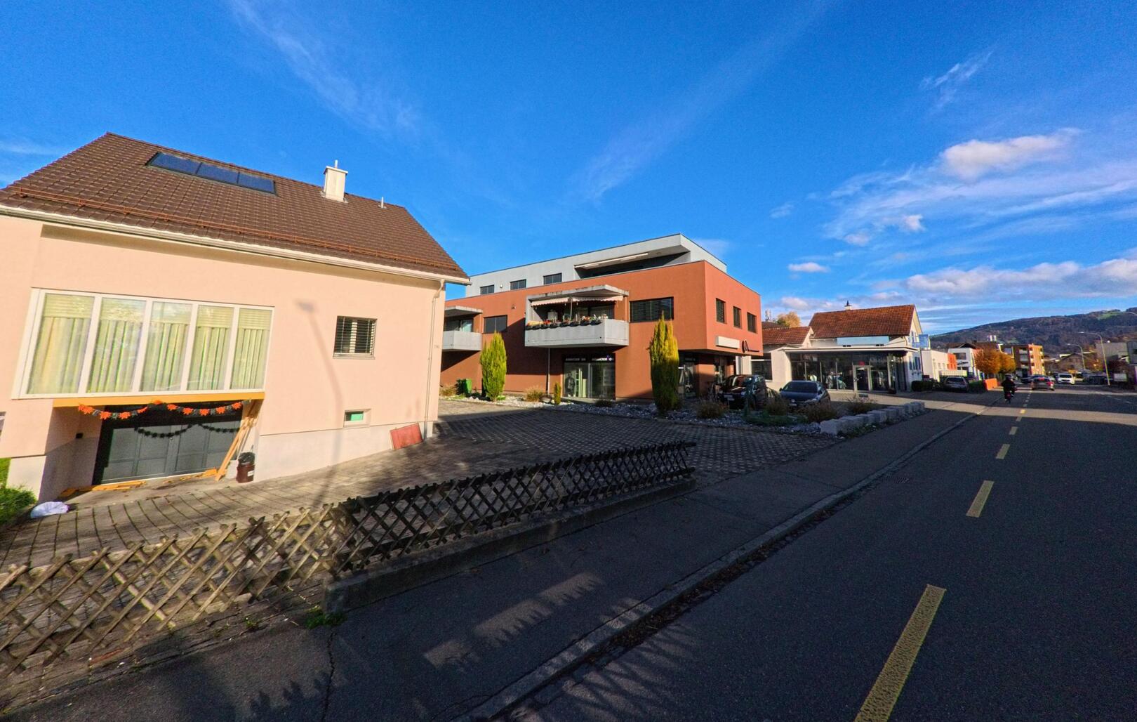 Entlang einer ruhigen Strasse in Widnau (9443, Kanton St. Gallen) stehen Wohnhaeuser und Gewerbebauten unter blauem Himmel mit freier Sicht auf die Umgebung.