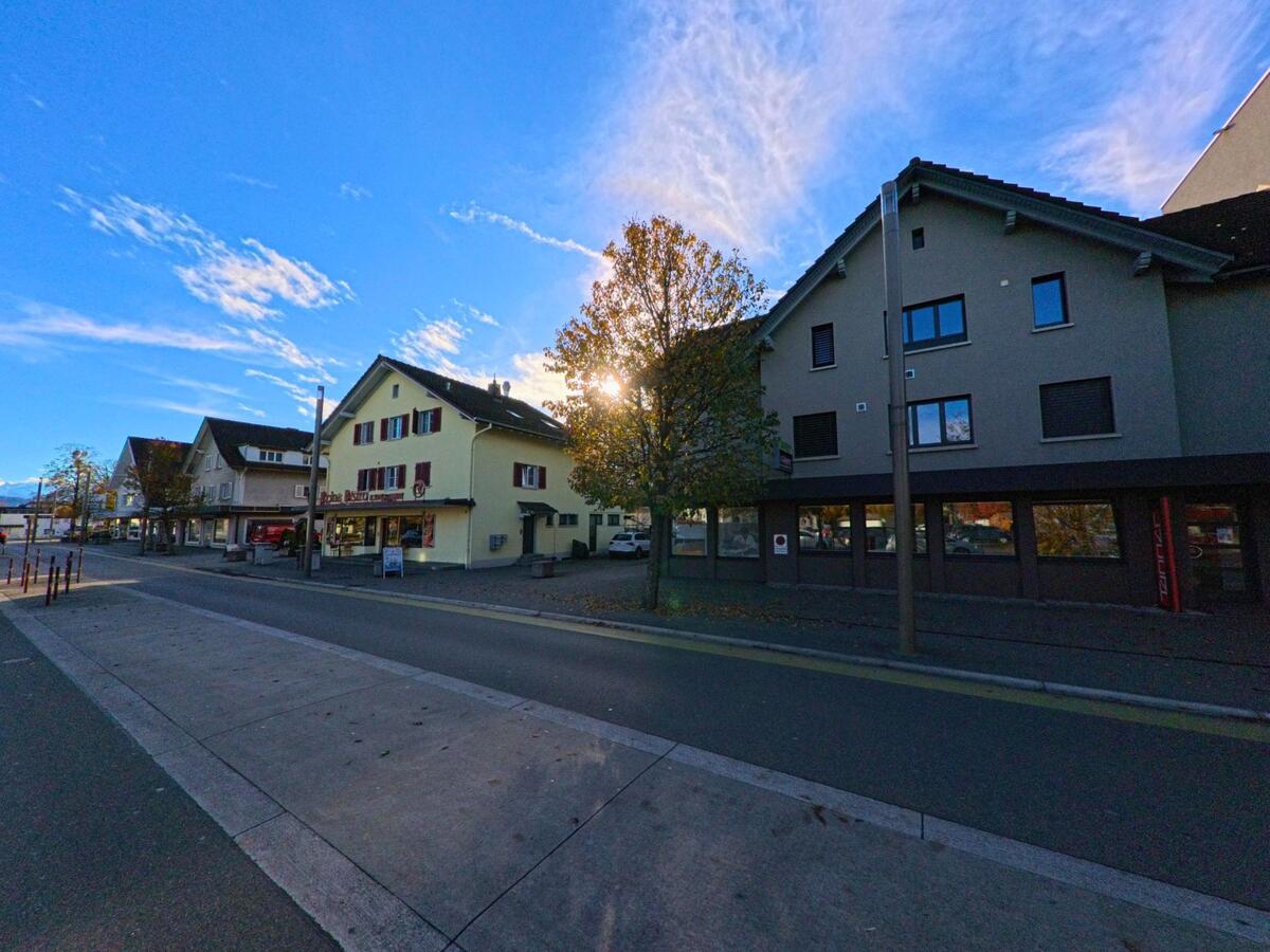 Entlang einer zentralen Strasse mit Geschäften und Wohnhäusern zeigt sich das Ortsbild von Widnau (9443, Kanton St. Gallen) im warmen Licht eines klaren Herbsttages.