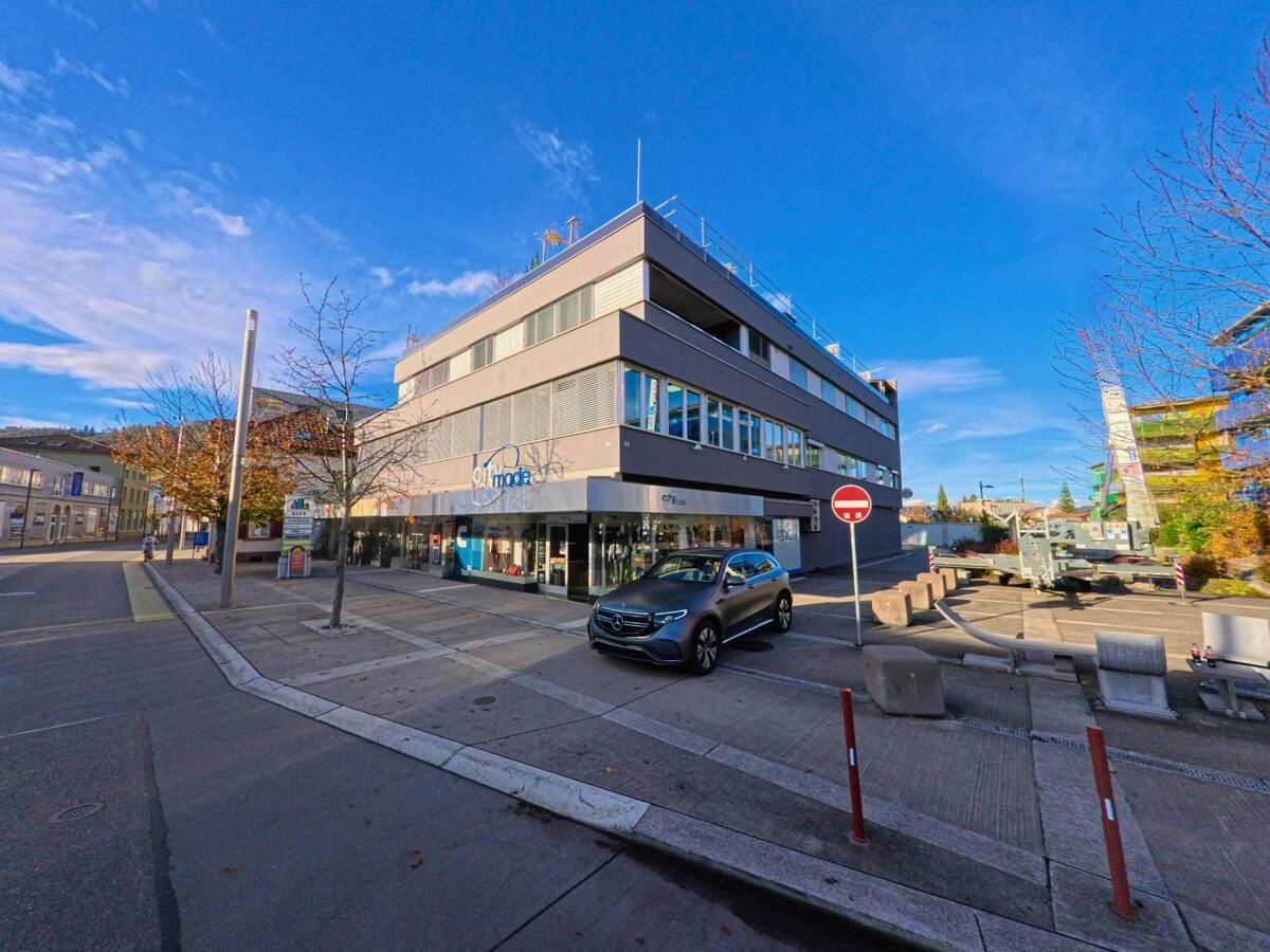 Ein markantes Geschäftsgebäude mit Läden im Erdgeschoss und breitem Gehbereich befindet sich zentral in Widnau (9443, Kanton St. Gallen) unter klarem Himmel.