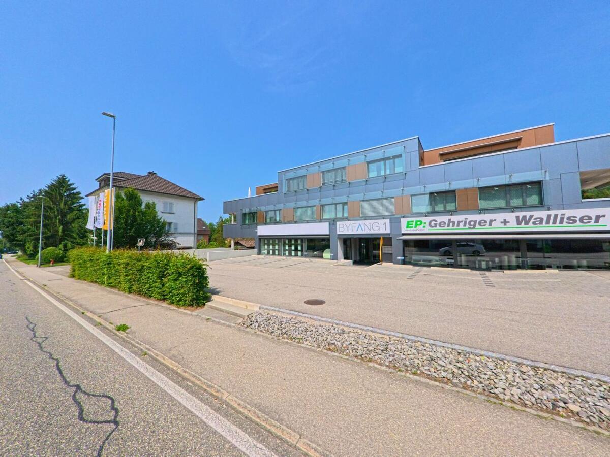 In Wiedlisbach (4537, Kanton Bern) steht ein modernes Geschaeftsgebaeude mit grossen Glasflaechen an einer ruhig verlaufenden Strasse.