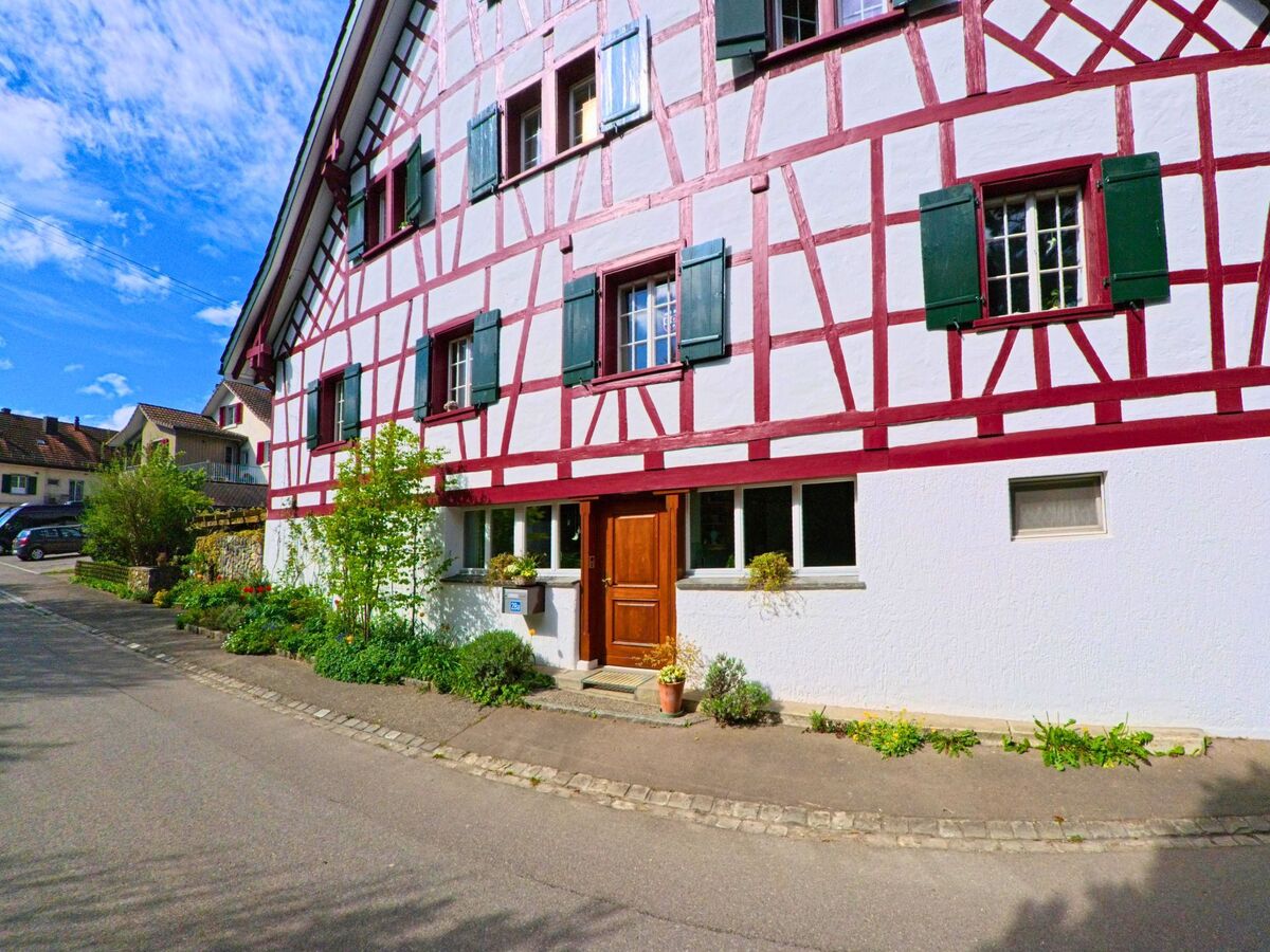 In Wiesendangen (8543, Kanton Zürich) zeigt das Bild ein traditionelles Fachwerkhaus mit einer weißen Fassade und roten Holzbalken sowie einem gepflegten Gartenbereich.