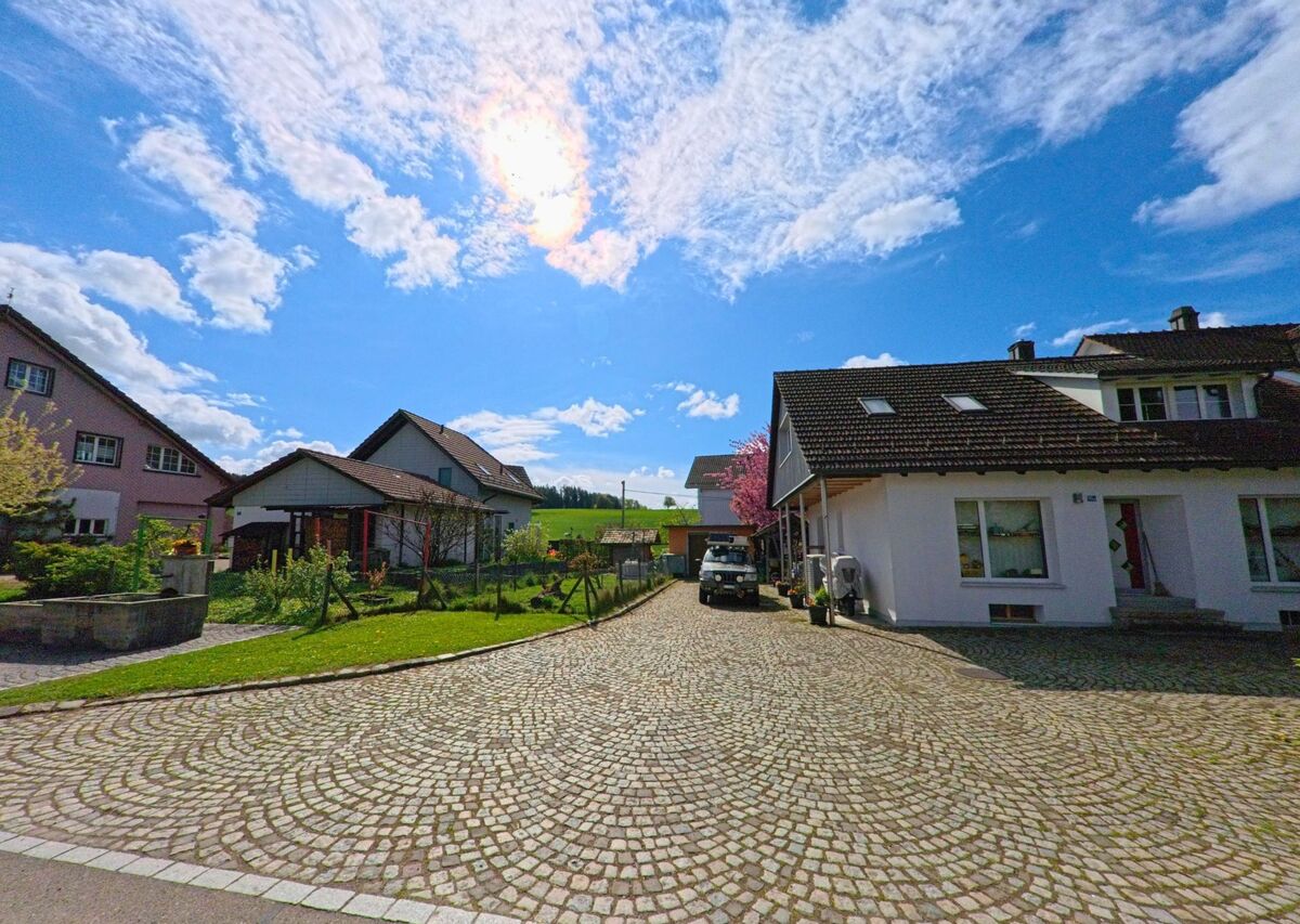 In einem Wohnquartier von Wiesendangen (8543, Kanton Zürich) führt ein gepflasterter Weg an gepflegten Einfamilienhäusern entlang in Richtung offener Landschaft.