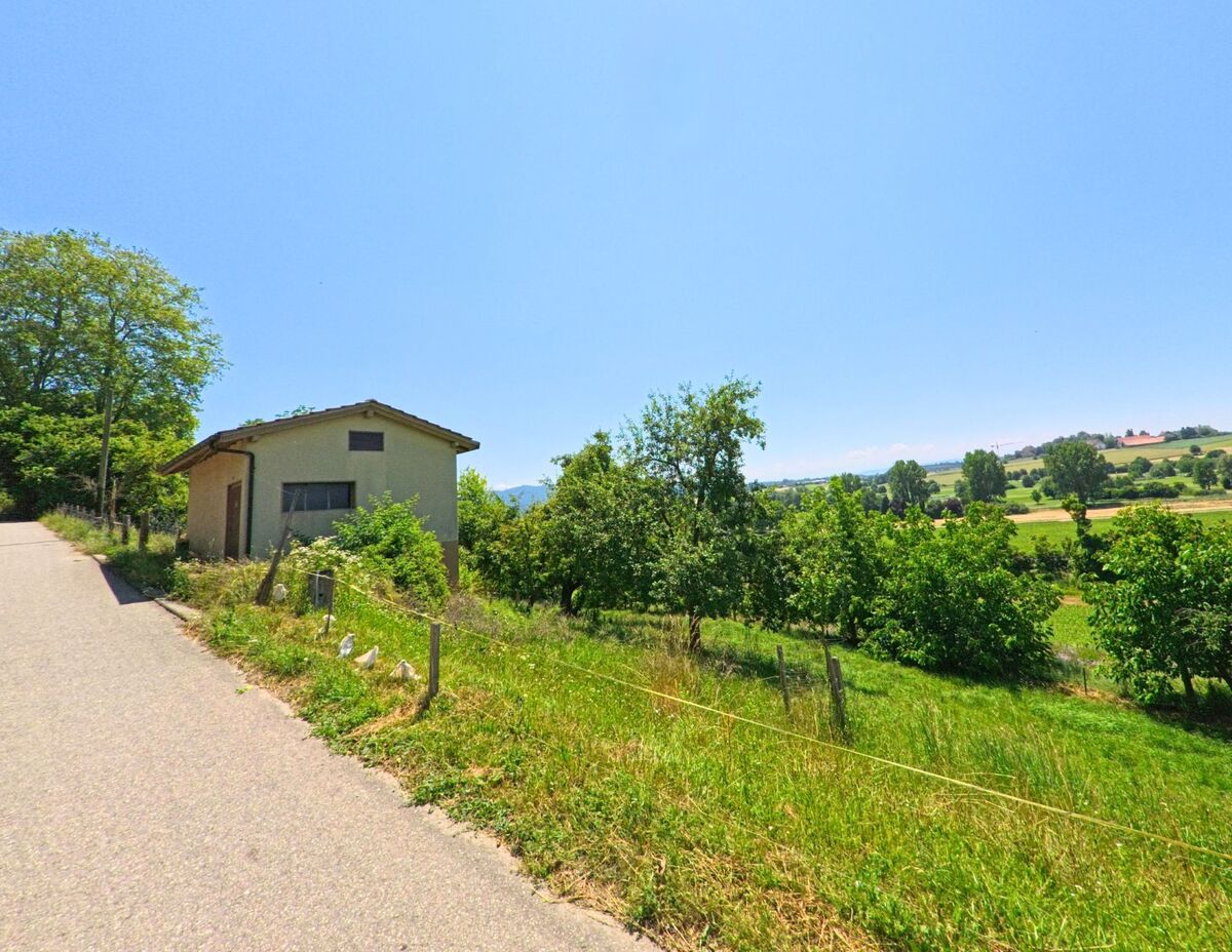 Ein kleines Gebäude an einem Hang in Wiggiswil (3053, Kanton Bern), mit einem weiten Blick auf grüne Felder und Bäume im Hintergrund.