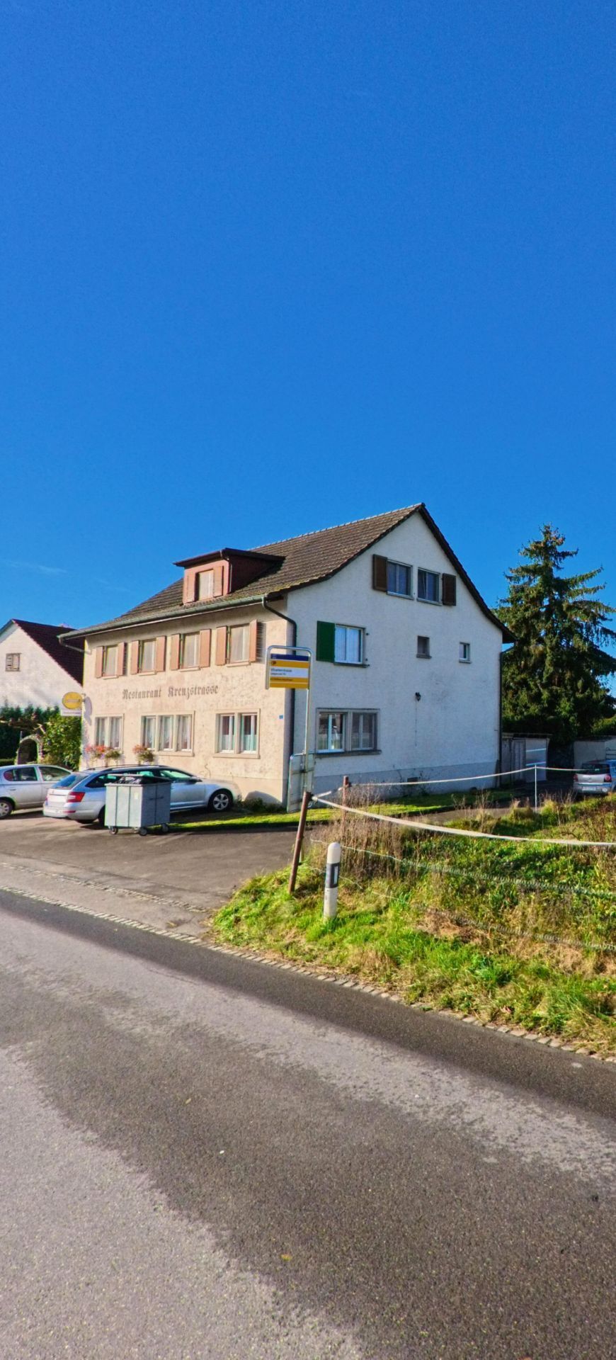 An einer Wegkreuzung in Wigoltingen (8556, Kanton Thurgau) zeigt das Bild eine Strassenszene mit Wegweisern, angrenzenden Gebaeuden und offenen Gruenflaechen am Dorfrand.