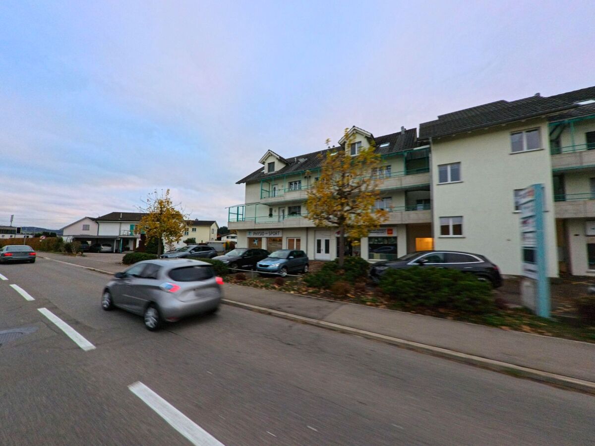 Entlang einer Hauptstrasse mit parkierenden Fahrzeugen und Gewerberaeumen zeigt sich ein gemischtes Wohn- und Geschaeftsgebaeude in Wilen (9535, Kanton Thurgau) bei ruhigem Verkehr.