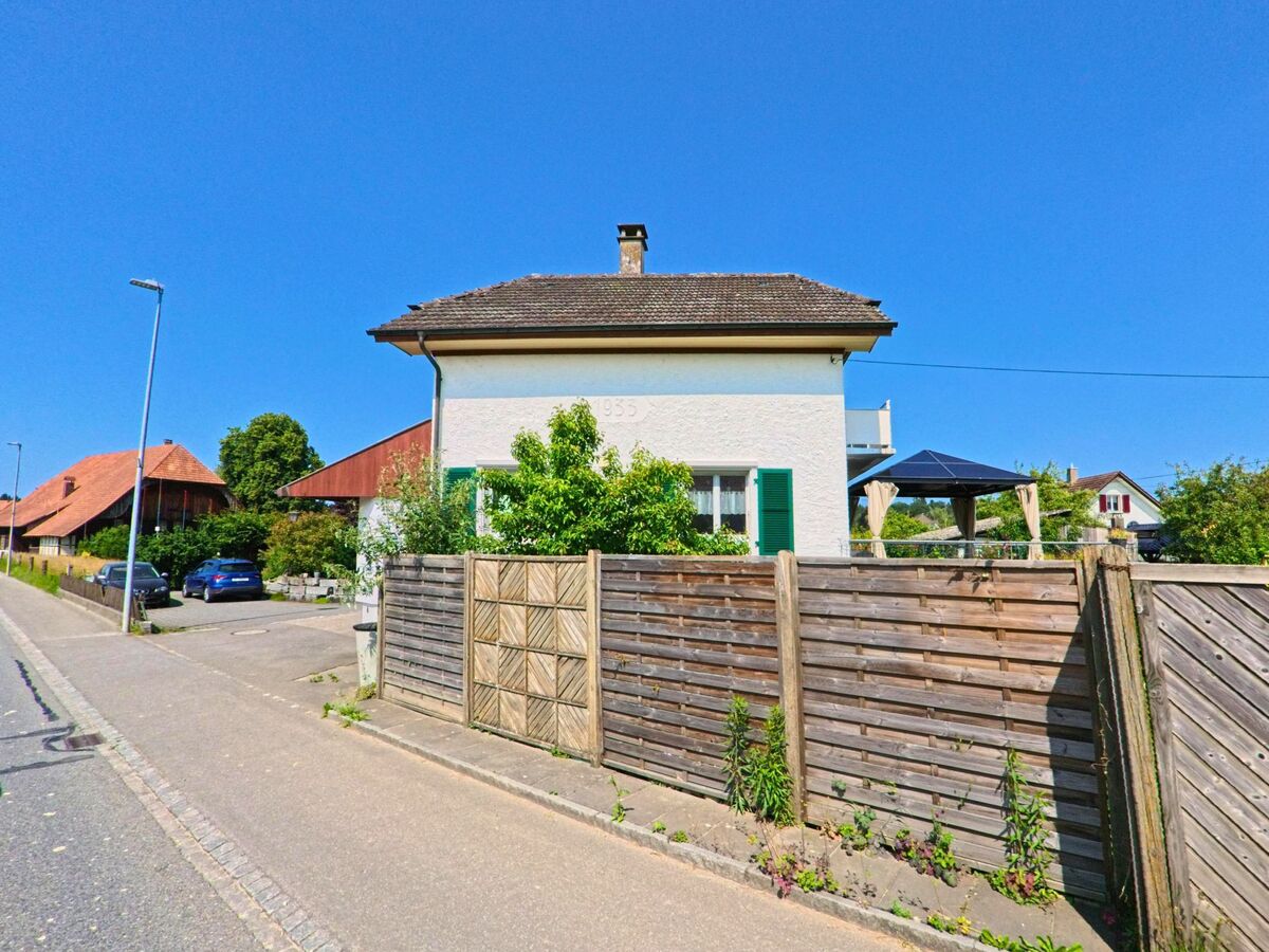 In Wiler bei Utzenstorf (3428, Kanton Bern) steht ein helles Wohnhaus mit grünen Fensterläden und Baujahr 1935, umgeben von einem Holzzaun und einem gepflegten Vorgarten.