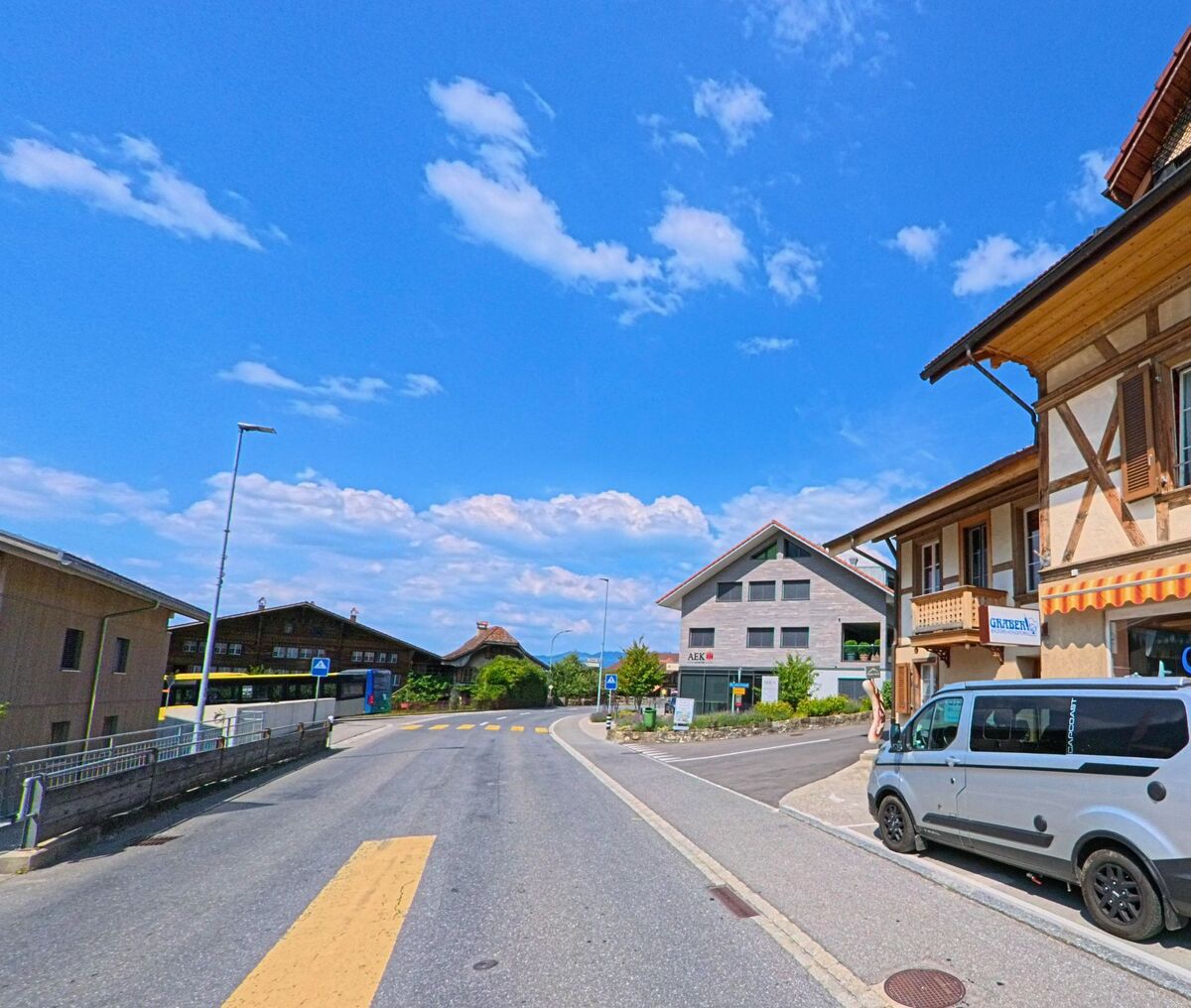In Wimmis (3752, Kanton Bern) markiert eine gelbe Fussgängerzone den Übergang zwischen einem Bushalt mit Holzgebäude und einem modernen Verwaltungsbau.