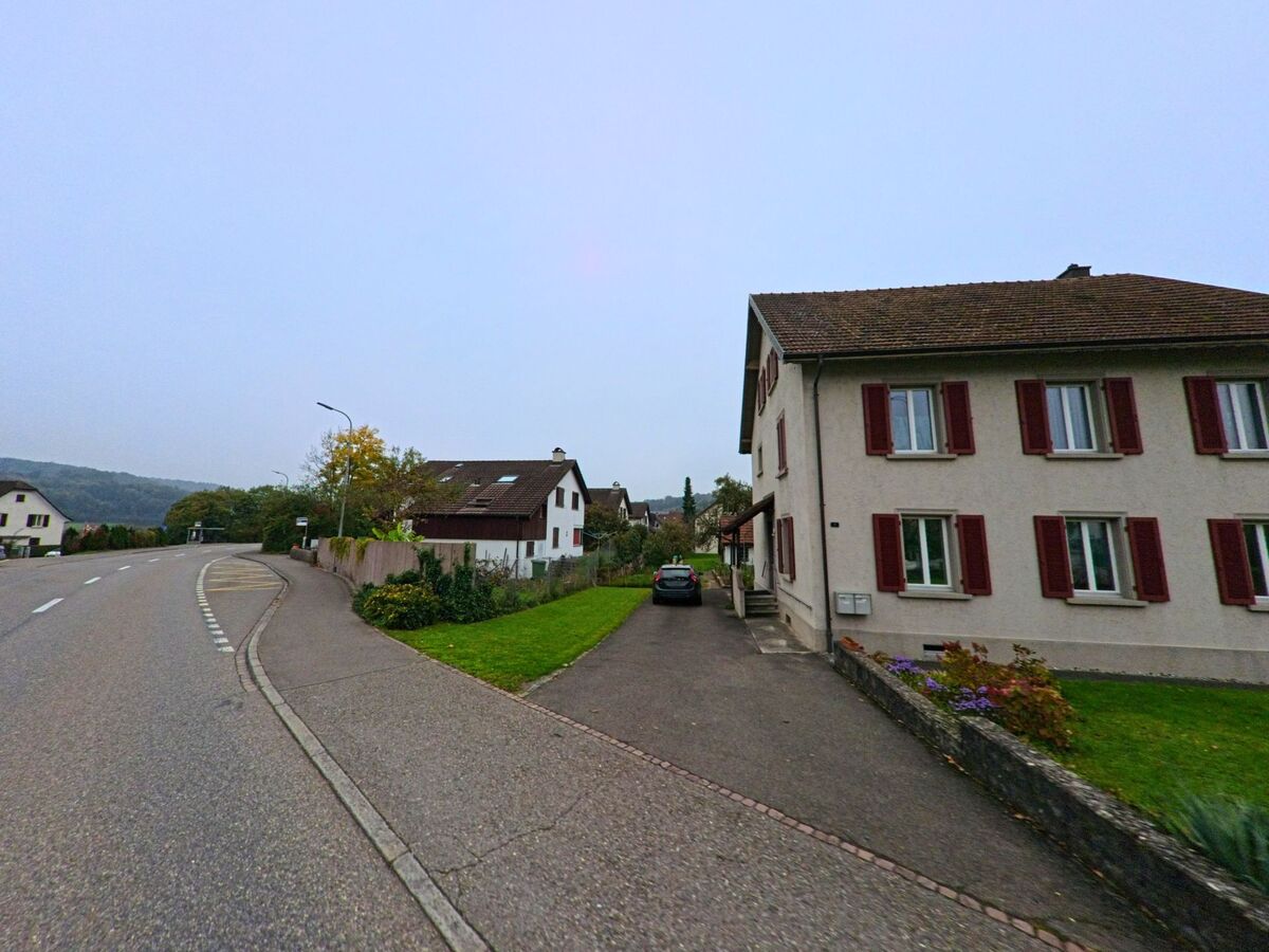 Ein ruhiger Strassenabschnitt in Windisch (5210, Kanton Aargau) fuehrt an gepflegten Wohnhaeusern mit roten Fensterlaeden und kleinen Gaerten vorbei.