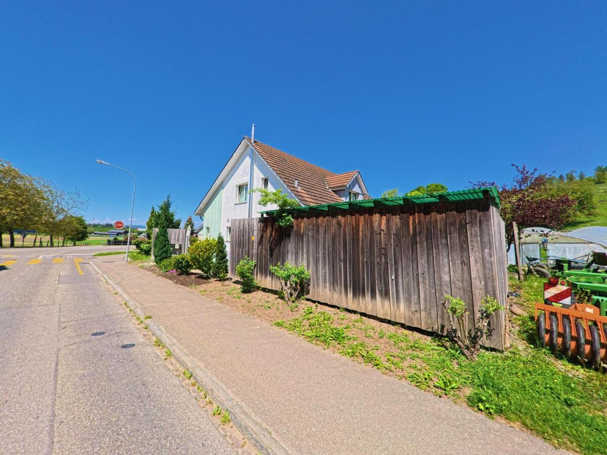 Ein Einfamilienhaus mit angrenzender Holzverschalung steht in Winkel, PLZ 8185 im Kanton Zürich, nahe einer ruhigen Strassenkreuzung mit Blick ins Grüne..jpg