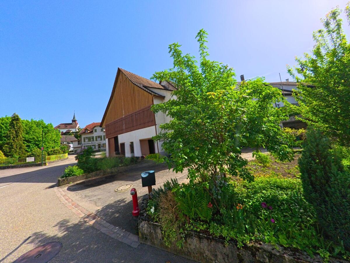 In Wintersingen (4451, Kanton Baselland) steht ein Fahrzeug mit Werbeaufschrift vor einem umgebauten Scheunengebaeude, im Hintergrund ist der Kirchturm des Dorfes sichtbar.