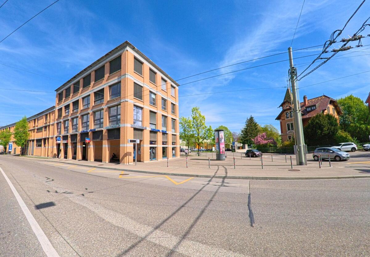 In Winterthur (8400, Kanton Zürich) steht ein modernes Buero- und Geschaeftsgebaeude aus rotem Backstein gegenueber einem historischen Wohnhaus mit Turm.