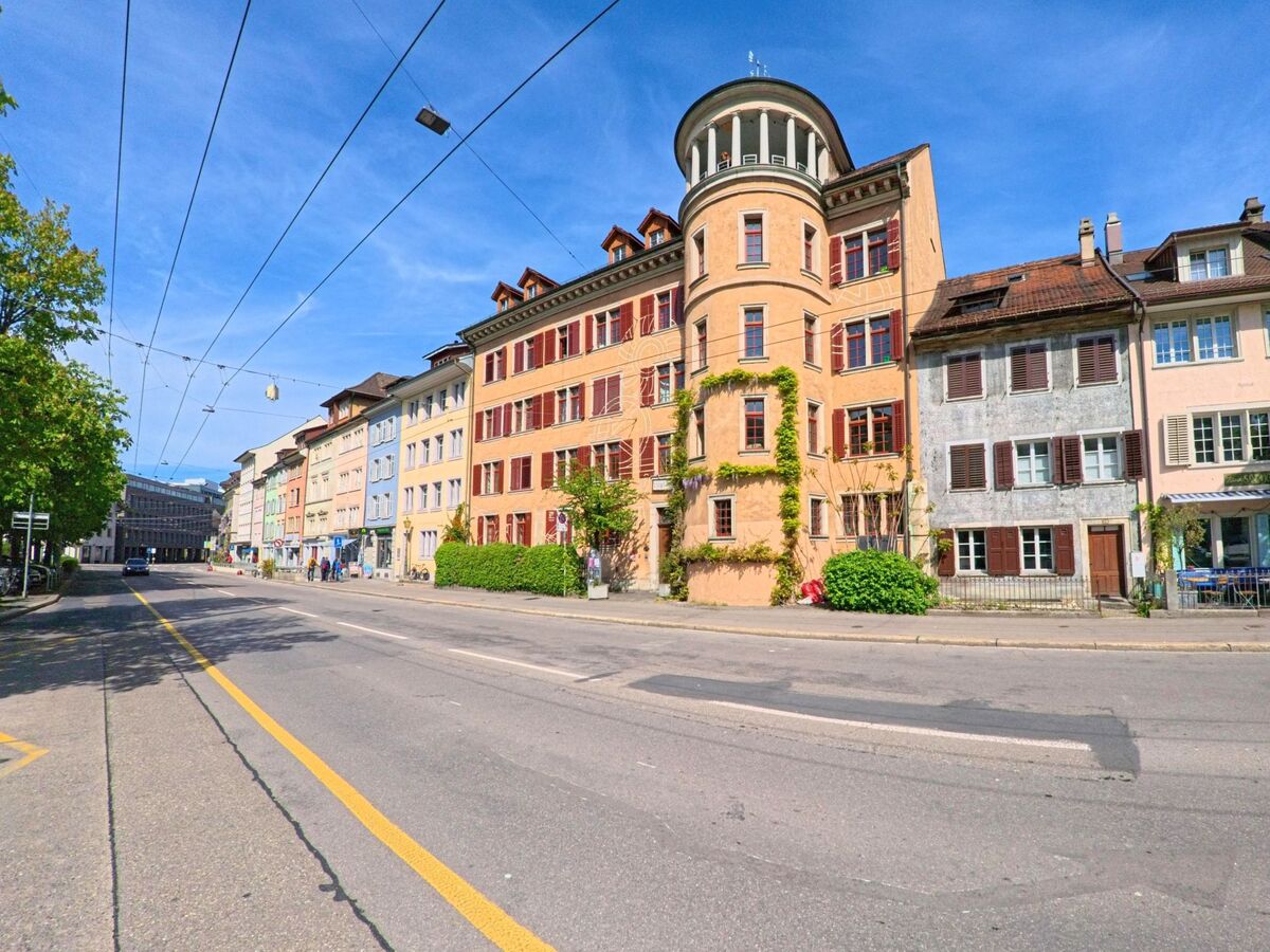 Entlang einer Hauptstrasse in Winterthur (8403, Kanton Zürich) stehen farbige historische Wohn- und Geschaeftshaeuser, darunter ein markantes Gebaeude mit rundem Turmaufsatz.