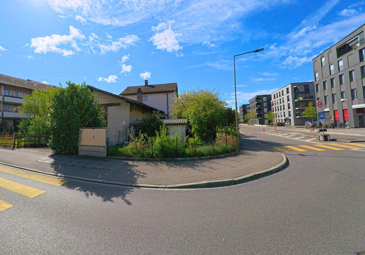 An einer Kreuzung in Winterthur (8404, Kanton Zürich) treffen Wohnhaeuser und moderne Apartmentgebaeude aufeinander, getrennt durch mehrere Fussgaengerstreifen.