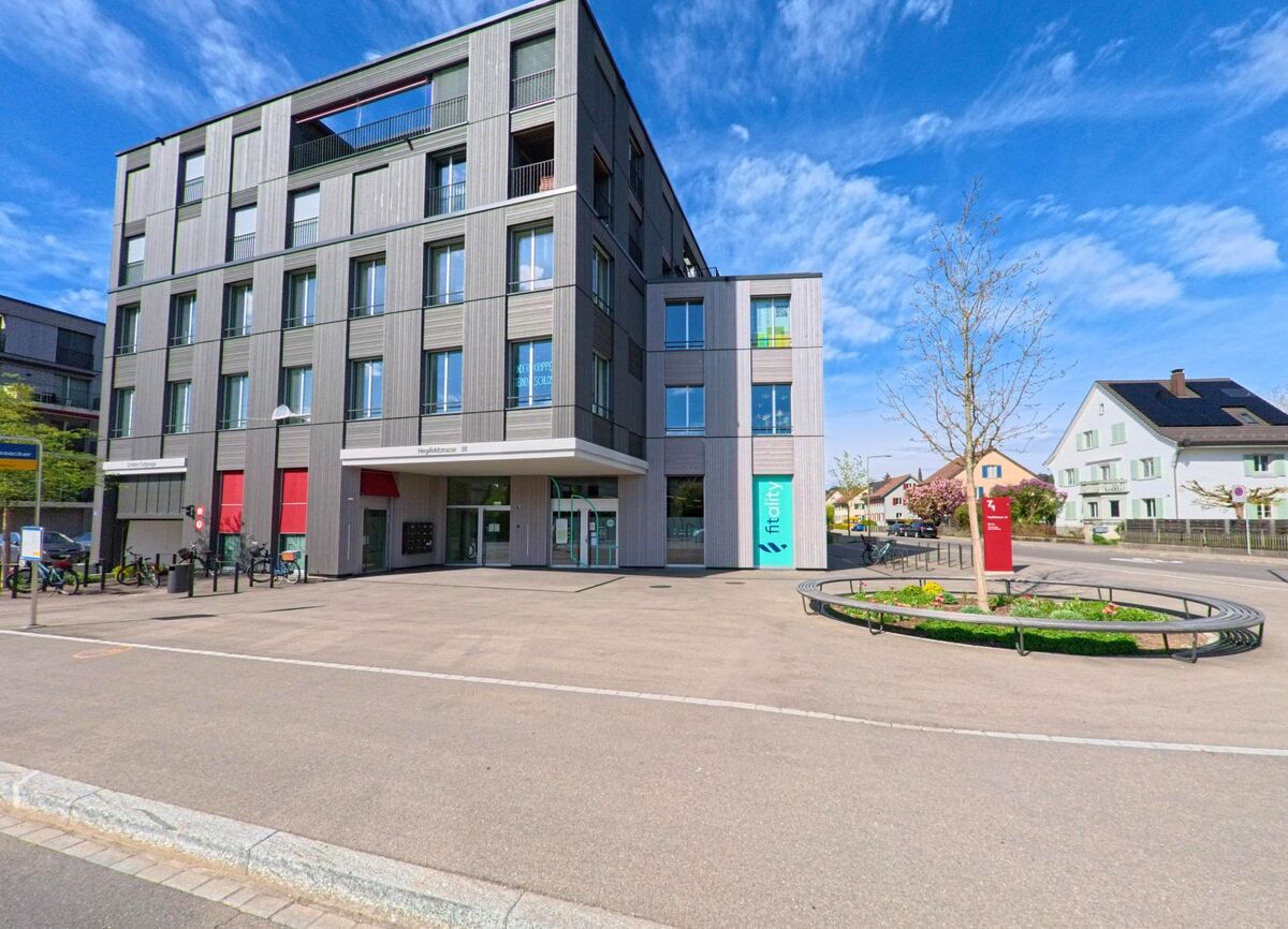 Ein modernes mehrstöckiges Gebaeude in Winterthur (8404, Kanton Zürich) steht an einer Strassenecke mit einem kleinen bepflanzten Rundplatz.