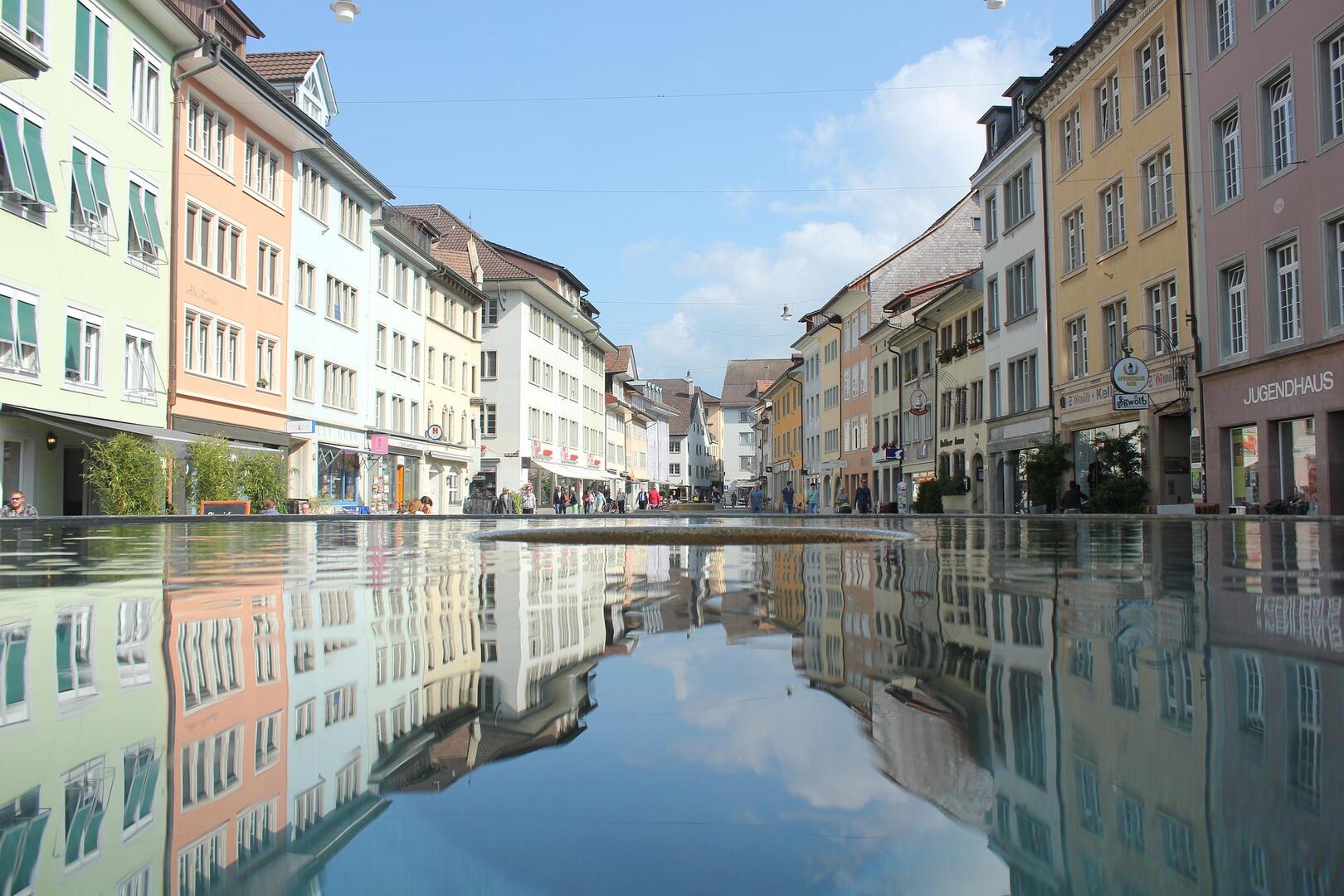 In Winterthur (8400, Kanton Zuerich) zeigt das Bild eine sonnige Kreuzung mit Wohn- und Buerohaeusern sowie einem markierten Fussgaengeruebergang.