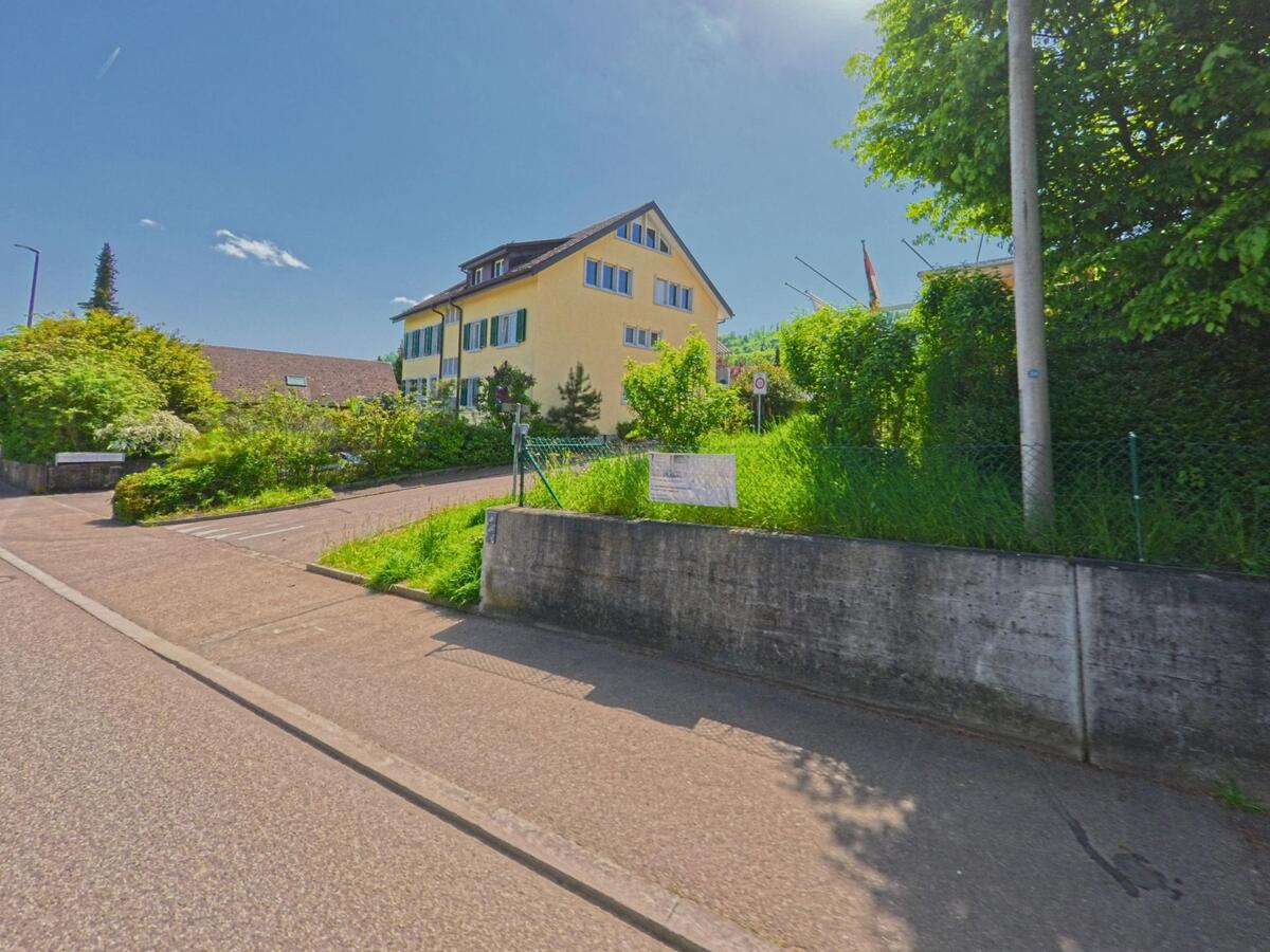 In Witterswil (4108, Kanton Solothurn) steht ein mehrstöckiges gelbes Gebäude mit Fensterläden an einer leicht ansteigenden Strasse im Grünen.