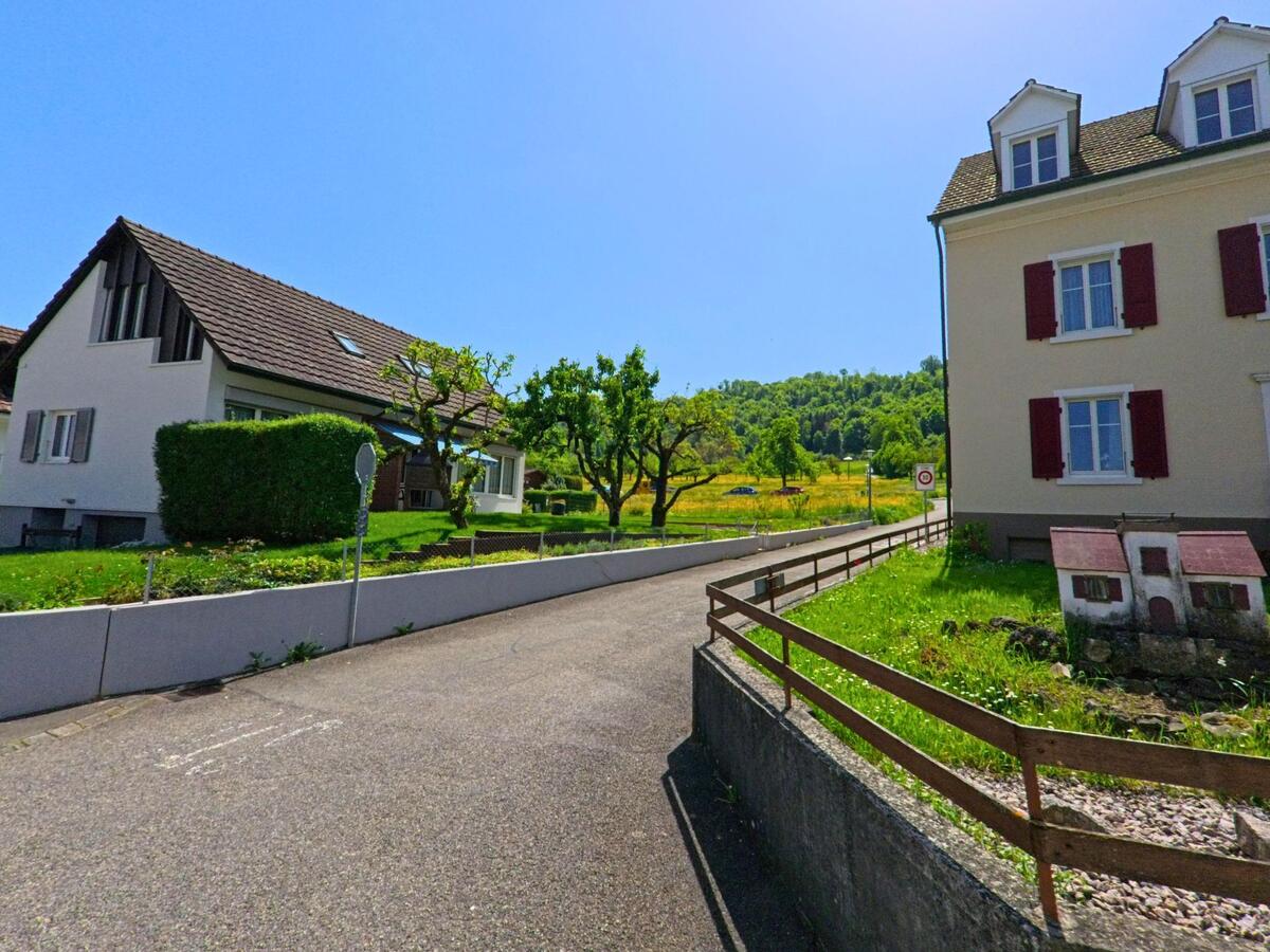  In Witterswil (4108, Kanton Solothurn) führt eine kleine Nebenstrasse an gepflegten Wohnhäusern vorbei in Richtung einer offenen Wiesenlandschaft.