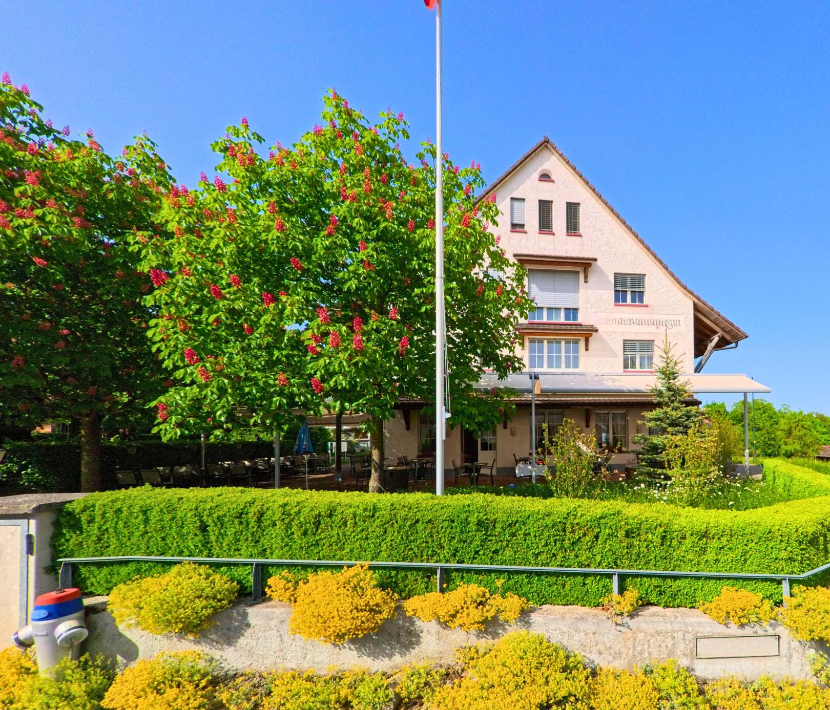 In Wittinsburg (4443, Kanton Baselland) steht das Restaurant zur Buche am Hinterhagweg, umgeben von blühenden Kastanien und einer gepflegten Gartenanlage.