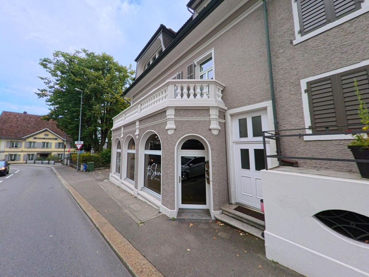 Ein elegantes Gebäude mit Rundbogenfenstern und Balkon steht an einer Strasse in Wohlen (5610, Kanton Aargau), gegenüber ist ein traditionsreiches Gasthaus zu sehen.