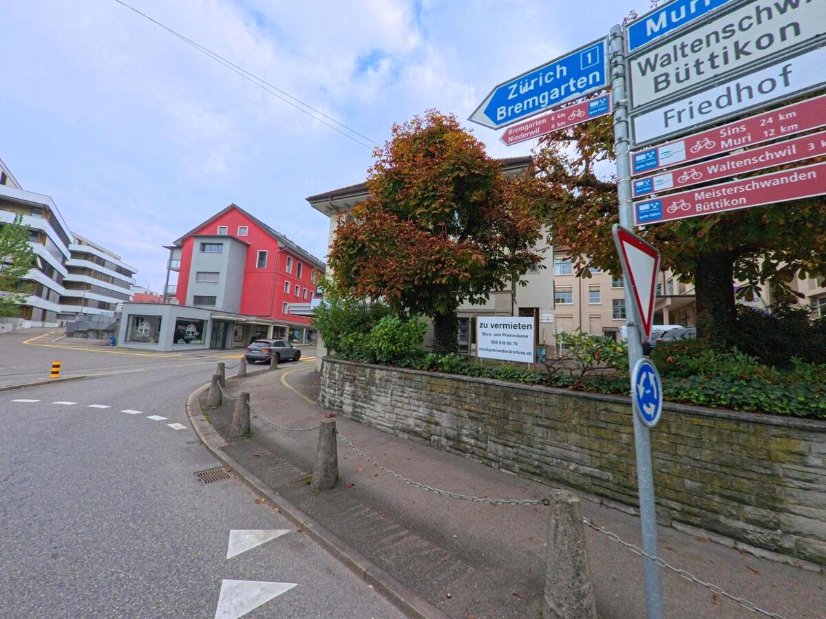 Mehrere Wegweiser zeigen an einer Strassenecke in Wohlen (5610, Kanton Aargau) Richtungen nach Zürich, Bremgarten und Muri, im Hintergrund stehen moderne Wohnhäuser.