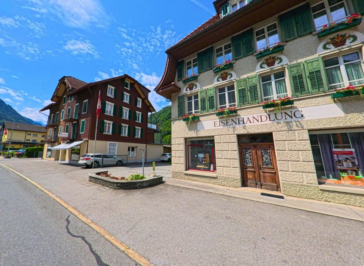 In der Ortsmitte von Wolfenschiessen (6386, Kanton Nidwalden) befindet sich ein traditionelles Geschaeftsgebäude mit der Aufschrift „Eisenhandlung“, geschmueckt mit Fensterlaeden und Blumen.