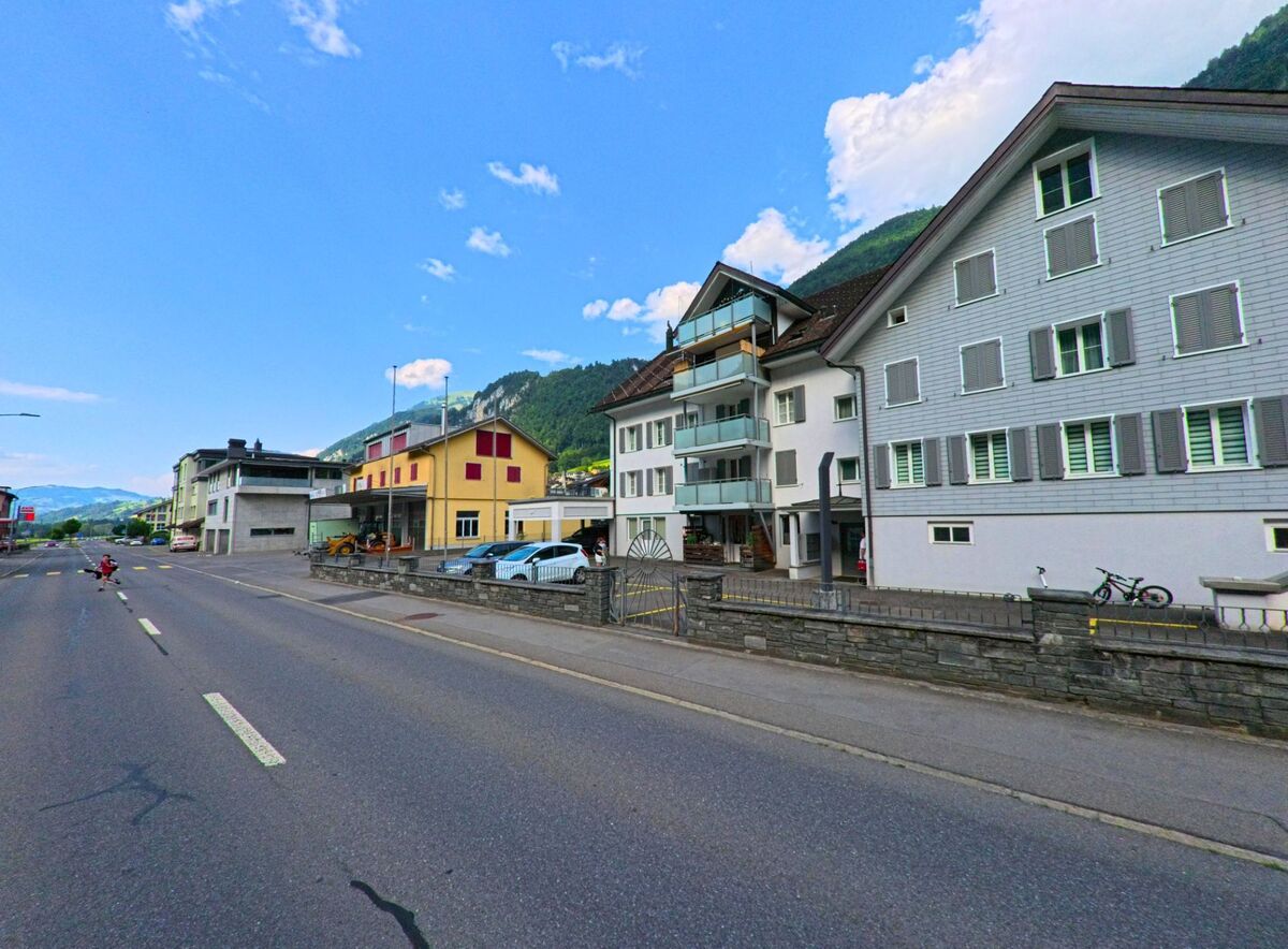 Entlang der Hauptstrasse von Wolfenschiessen (6386, Kanton Nidwalden) reihen sich Wohnhaeuser, Gewerbebauten und Werkstaetten vor bewaldeter Bergkulisse aneinander.