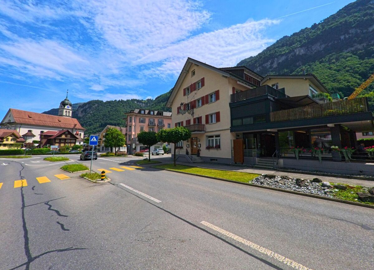 Eine zentrale Kreuzung in Wolfenschiessen (6386, Kanton Nidwalden) wird von Gasthaeusern, Wohngebaeuden und der markanten Kirche mit Zwiebelturm eingerahmt.