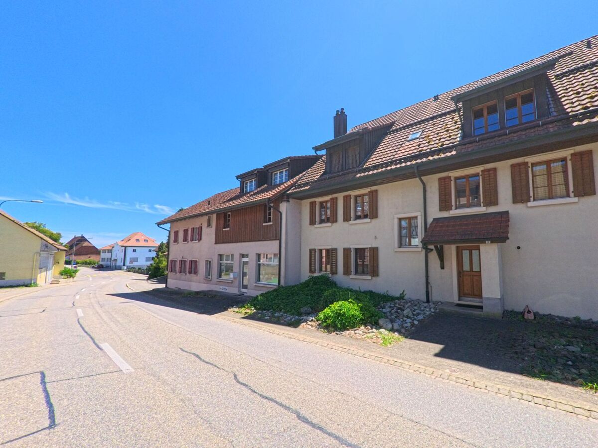 Entlang einer sanft geschwungenen Strasse in Wolfwil (4628, Kanton Solothurn) reihen sich gepflegte Häuser mit Fensterläden und Ziegeldächern.